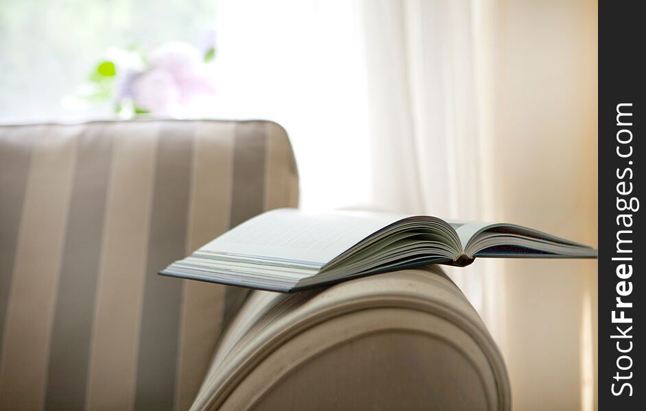 Book on the chair behind the window in a white cosy interior. vintage style with modern interior style and brown sofa