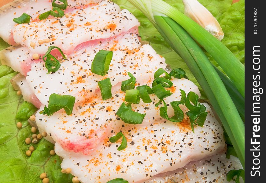 It is thin the cut slices of fat on a plate and decorated with the crushed green onions. It is thin the cut slices of fat on a plate and decorated with the crushed green onions