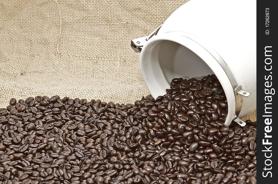 Whole roasted organic coffee beans, evenly spilling out of an urn on a brown burlap background, with an urban vintage retro chic feel. Whole roasted organic coffee beans, evenly spilling out of an urn on a brown burlap background, with an urban vintage retro chic feel.