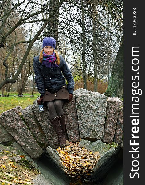 A girl in an autumn city park sits on stone rails. A girl in an autumn city park sits on stone rails