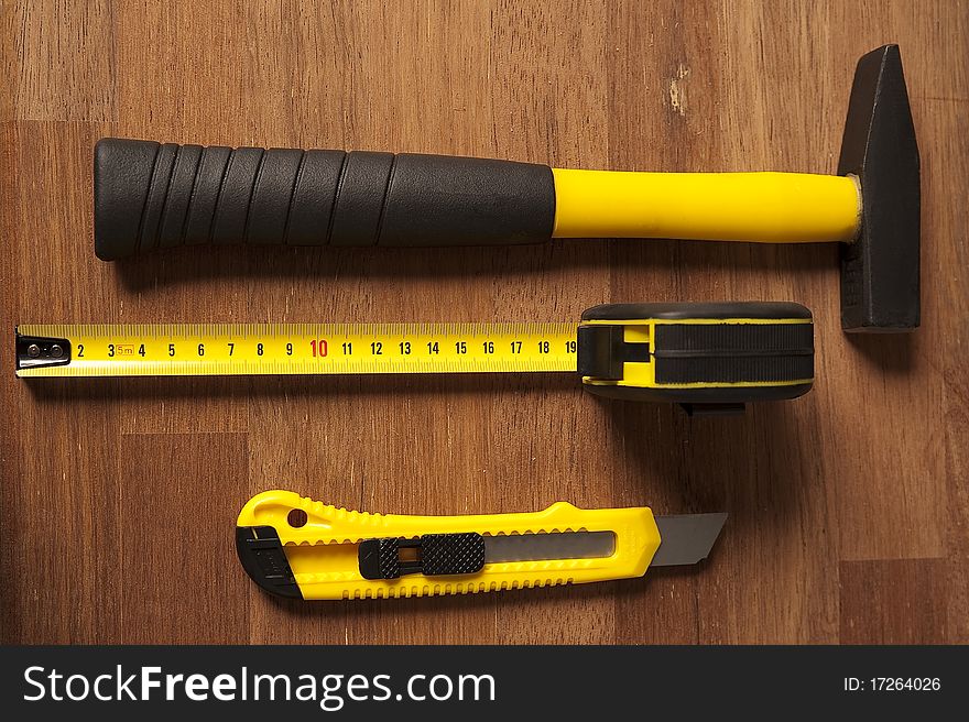 Image shows a composition of three tools. All are black/yellow. They are lied on brown wood. Image shows a composition of three tools. All are black/yellow. They are lied on brown wood.