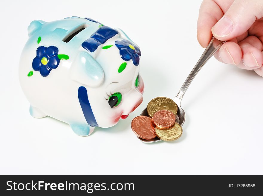 Male hand feeding a colorful piggy bank with a coins in spoon. Male hand feeding a colorful piggy bank with a coins in spoon