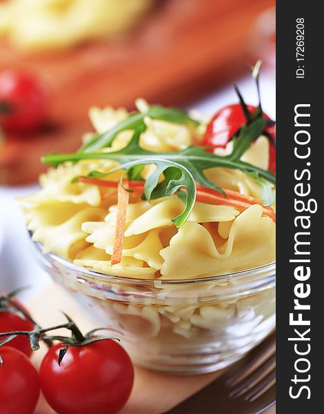 Bowl of bowtie pasta garnished with arugula and carrot