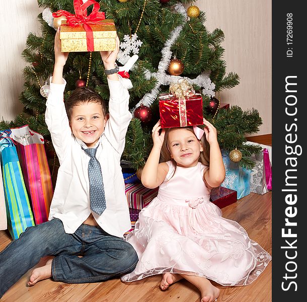 Merry girl and boy with gifts near a new-year tree. Merry girl and boy with gifts near a new-year tree