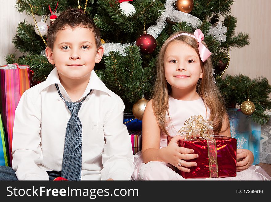 Merry girl and boy with gifts near a new-year tree. Merry girl and boy with gifts near a new-year tree