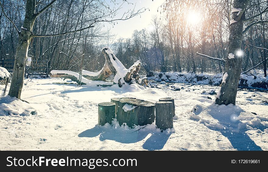 Winter snowing landscape  with clean white blue sky and a sharp sun lighting  a table and some chairs made of wooden , nearby a frozen river. Winter snowing landscape  with clean white blue sky and a sharp sun lighting  a table and some chairs made of wooden , nearby a frozen river