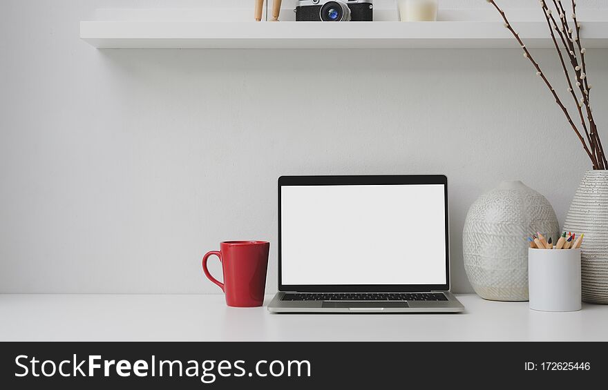 Cropped Shot Of Workplace With Blank Screen Laptop, Red Coffee Cup, Decorations On White Desk