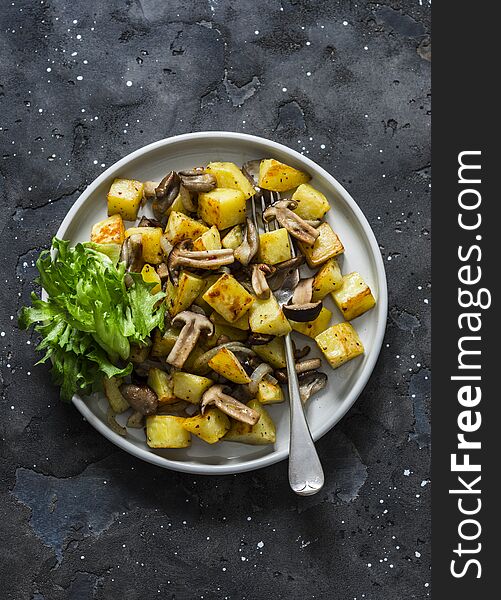 Fried potatoes with mushrooms and green salad - delicious simple vegetarian lunch on a dark background, top view