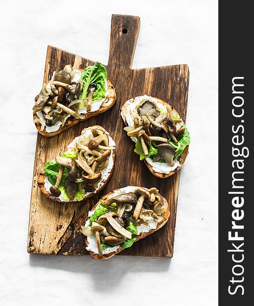 Mixed mushrooms cream cheese green salad on the grill bread sandwiches on a rustic cutting board on a light background, top view