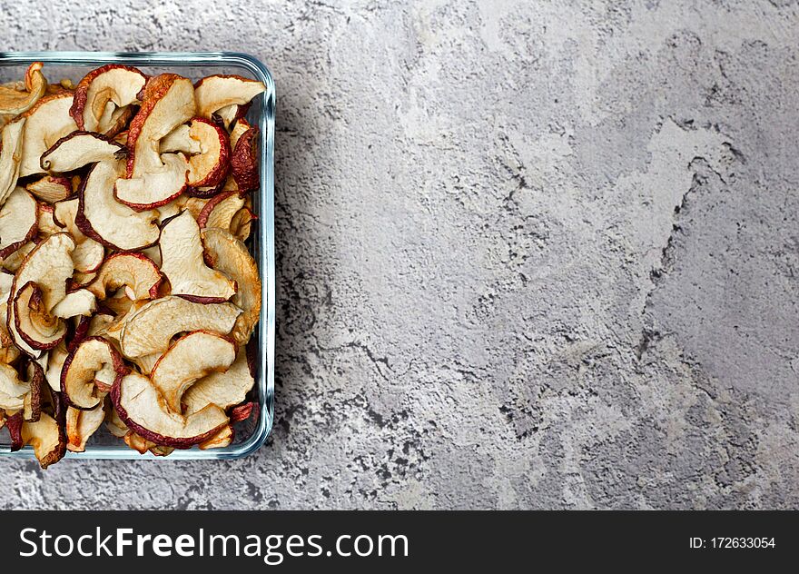 Dried Apple chips in a square glass plate on a gray concrete background. Organic natural food. Top view. Flat lay. Copy space.