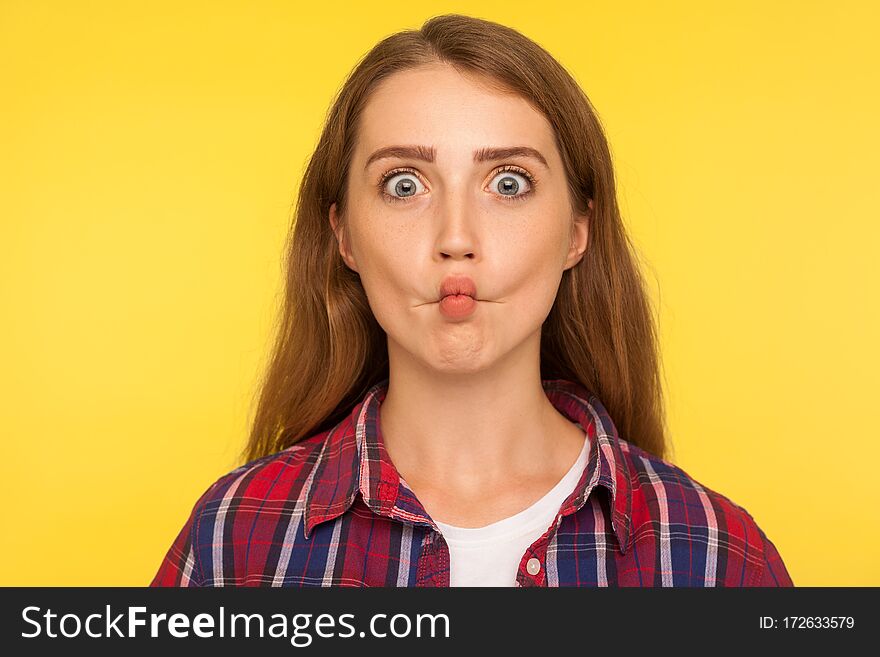 Portrait of amusing funny ginger girl in checkered shirt making fish face and looking with big eyes, confused ridiculous expression, comical wondered grimace. studio shot isolated on yellow background