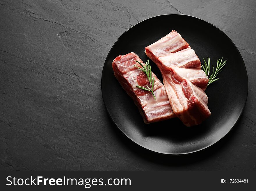 Raw ribs with rosemary on black table, top view