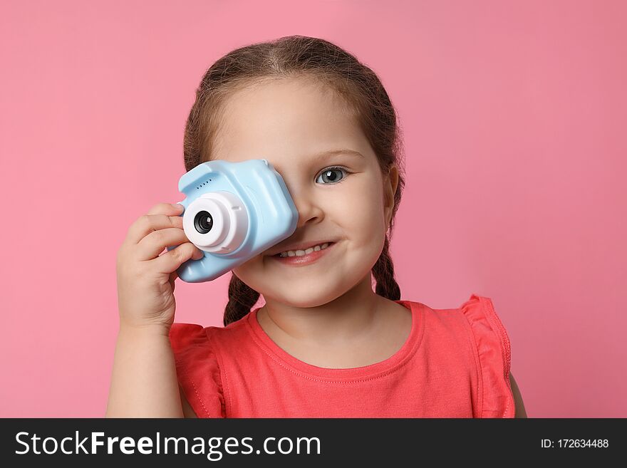 Little photographer taking picture with toy camera on pink background