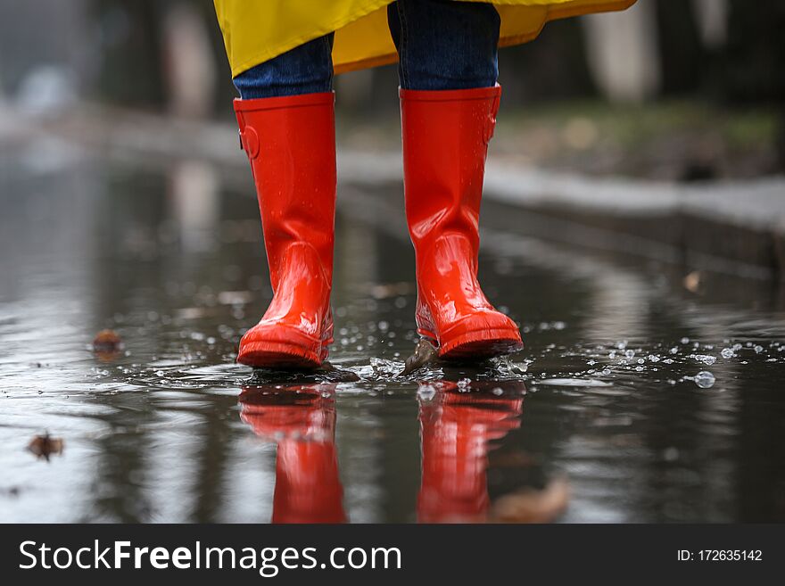 Woman jumping in puddle outdoors on rainy day, closeup