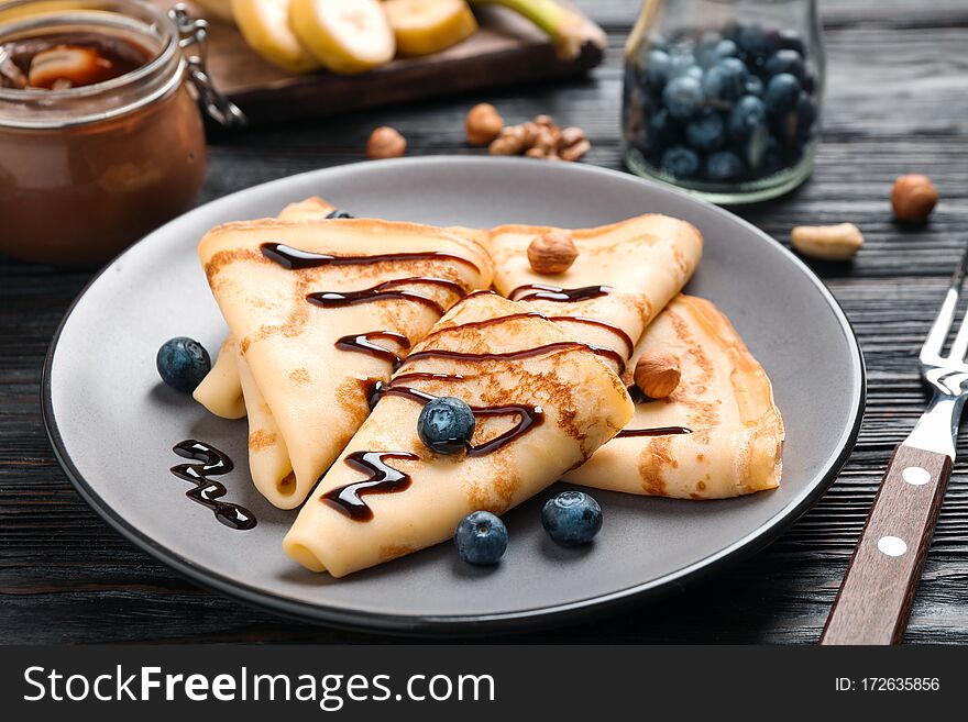 Delicious thin pancakes with chocolate, blueberries and nuts on black wooden table