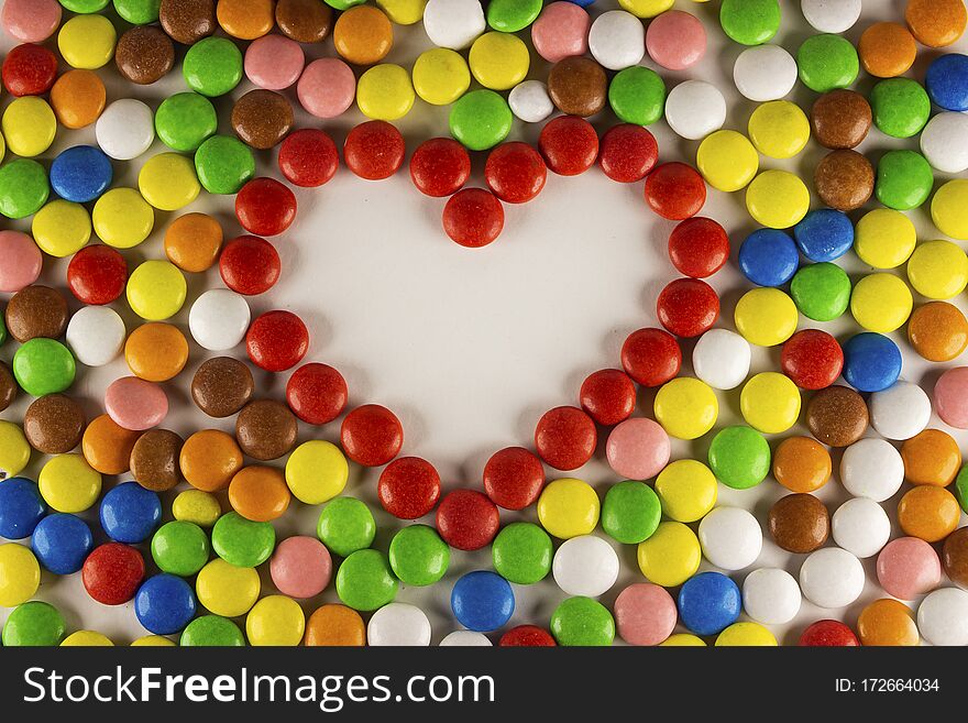 Colorful dragee beans in the shape of a heart on a white background. Decoration background. Closeup