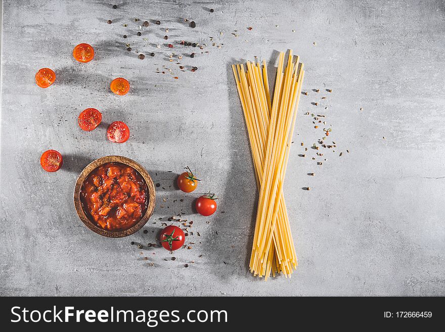 Tomato sauce with uncooked spaghetti on gray table