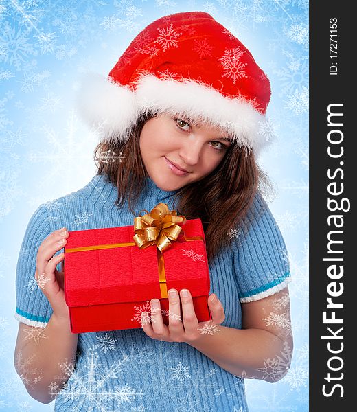 Smiling christmas girl holding gift wearing Santa hat. Blue background with snowflakes.