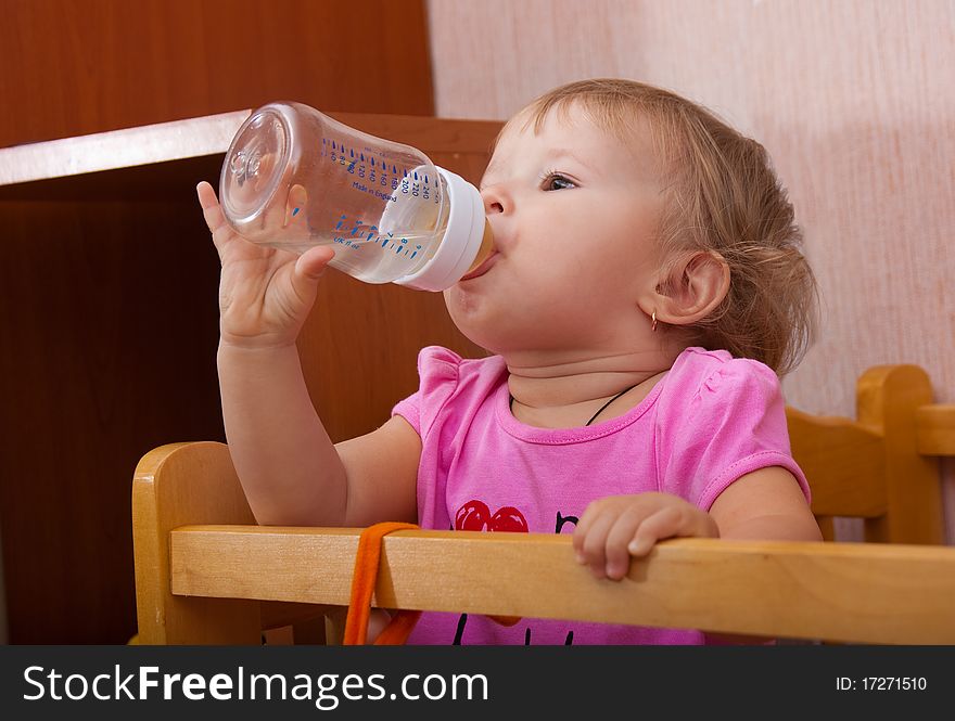 The small nice girl in a bed drinks itself from a small bottle. The small nice girl in a bed drinks itself from a small bottle