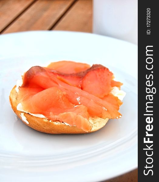 Bagel and Cream cheese topped with smoked salmon on a white plate at the breakfast table. Bagel and Cream cheese topped with smoked salmon on a white plate at the breakfast table