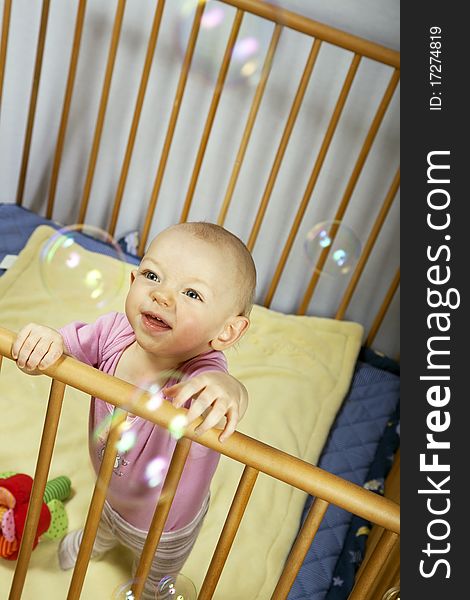 Little baby holds on to the baby bed and is happy about soap bubbles. Little baby holds on to the baby bed and is happy about soap bubbles