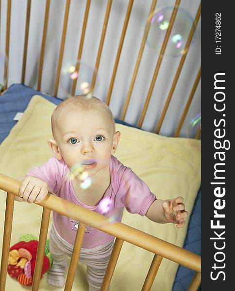 Little baby holds on to the baby bed and looks behind the bubbles. Little baby holds on to the baby bed and looks behind the bubbles