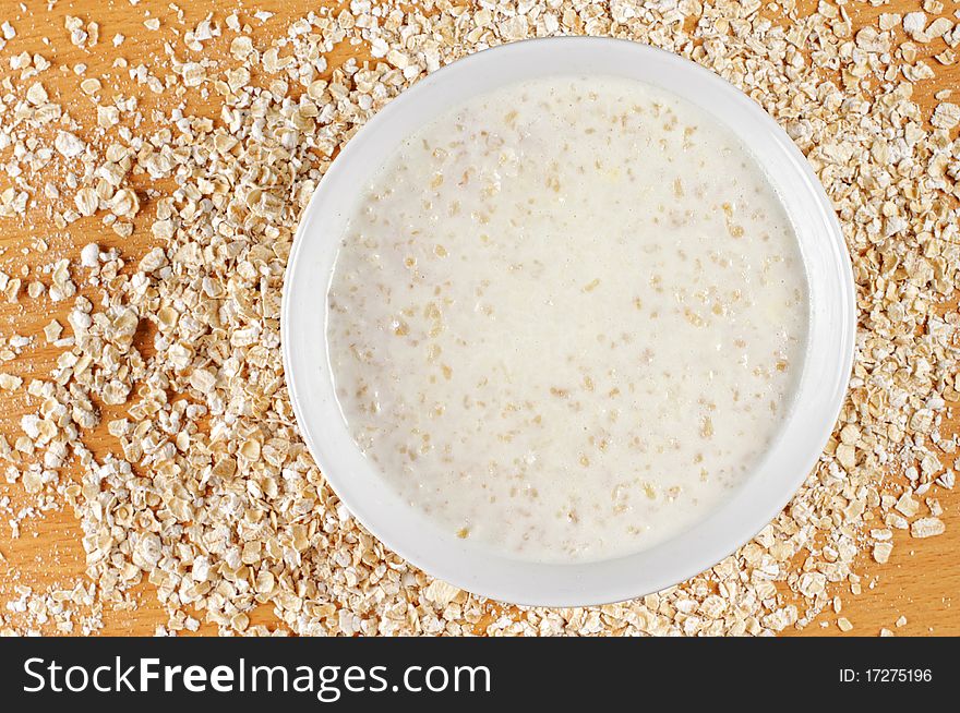 A big bowl of cooked oatmeal with oatmeal flakes from top point of view