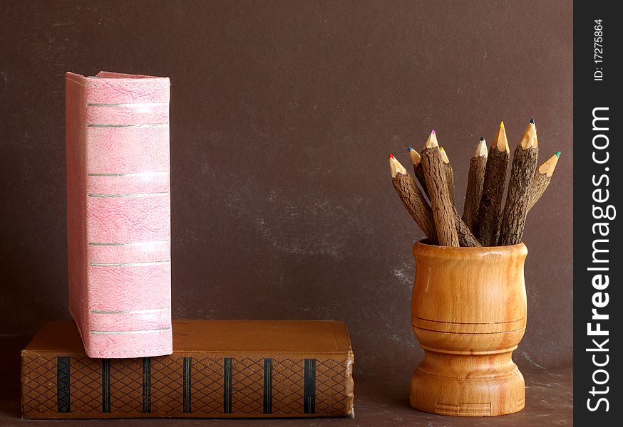 Old school books and wooden pencils on brown background