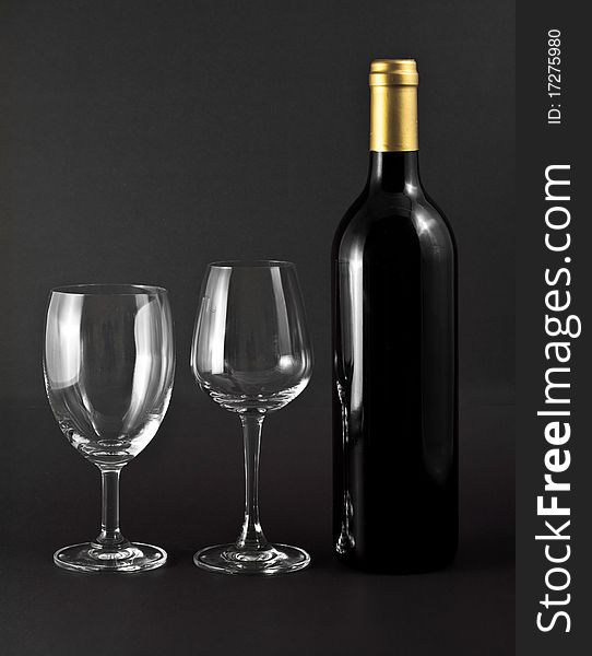 A bottle of red wine and two elegant glasses on black background