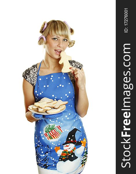 Pretty young woman in an apron and oven gloves holding a plate of gingerbread cookies for the little people christmas. Tries to bite one cookie. Lots of copyspace and room for text on this isolate. Pretty young woman in an apron and oven gloves holding a plate of gingerbread cookies for the little people christmas. Tries to bite one cookie. Lots of copyspace and room for text on this isolate