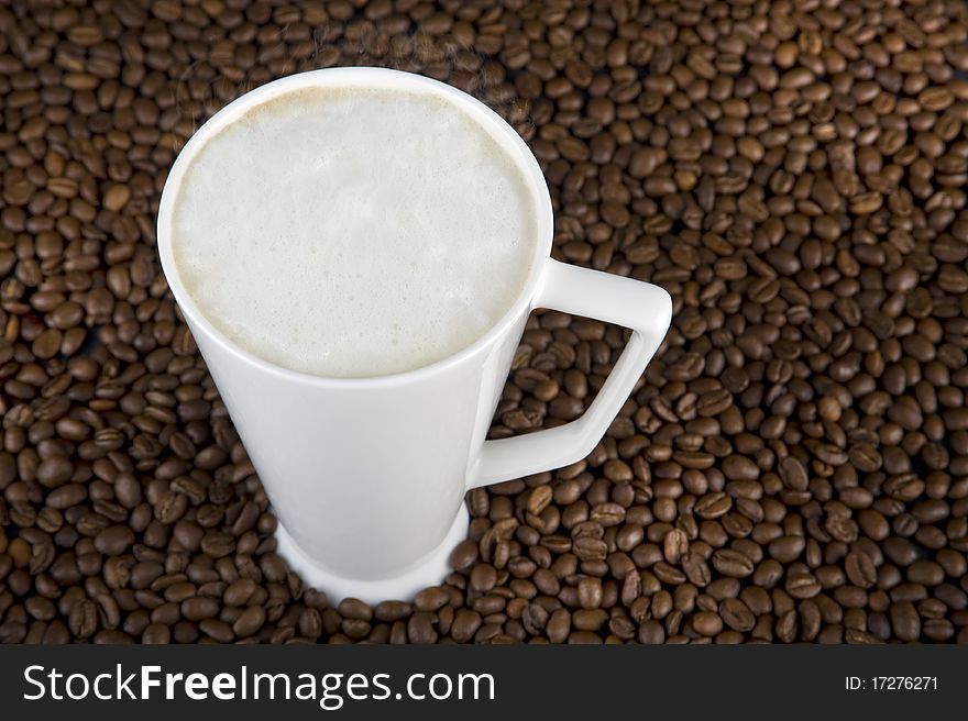 Coffee time - mug filled with hot coffe with cream on brown beans background. Coffee time - mug filled with hot coffe with cream on brown beans background