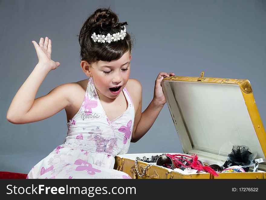 Little girl dressed as princess exclaims with surprise upon finding jewelry in a trunk. Little girl dressed as princess exclaims with surprise upon finding jewelry in a trunk.