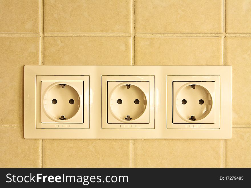 White triple power socket on tiled wall in kitchen