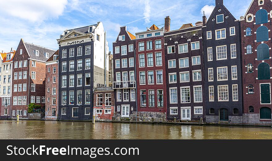 A row of leaning multi-story homes on a canal in Amsterdam appear to be dancing with each other as they lean into one another. A row of leaning multi-story homes on a canal in Amsterdam appear to be dancing with each other as they lean into one another.