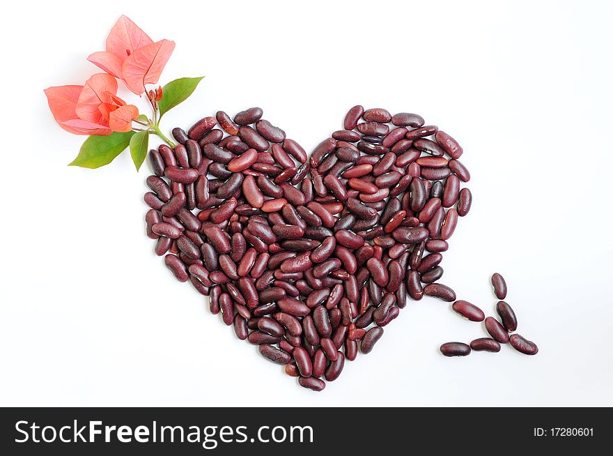 Heart made of beans with pink flowers and an arrow though on a white background