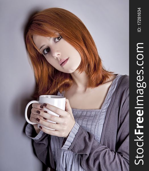 Portrait of red-haired girl with cup. Studio shot.
