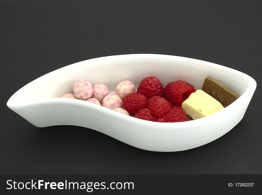 Raspberry, chocolates, and sweet balls on a white ceramic plate. Raspberry, chocolates, and sweet balls on a white ceramic plate