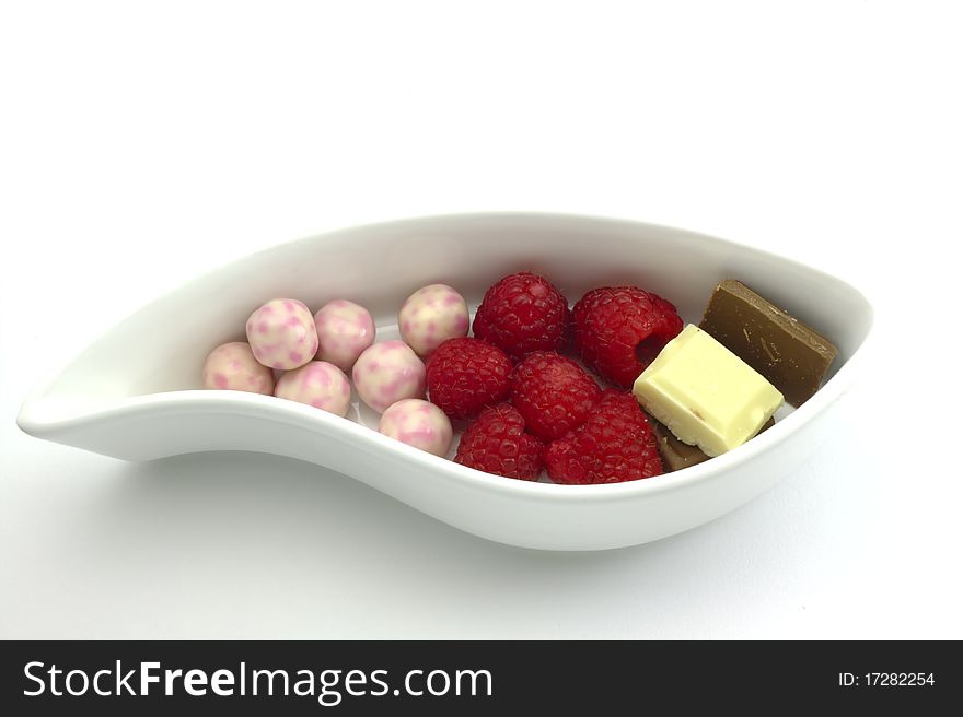 Raspberry, chocolates, and sweet balls on a white ceramic plate. Raspberry, chocolates, and sweet balls on a white ceramic plate