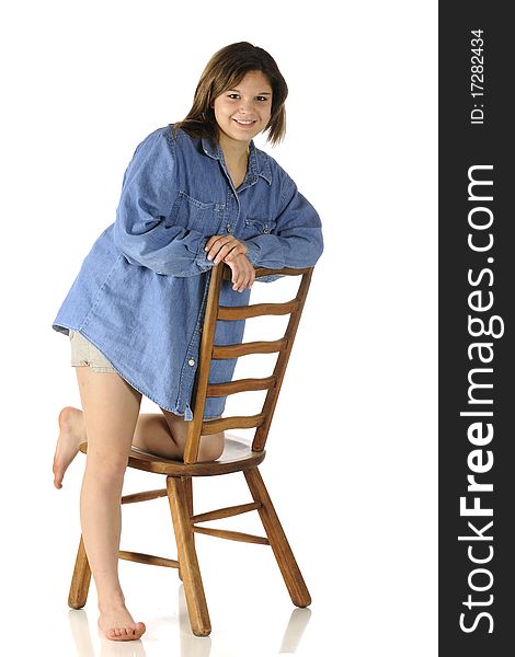 A beautiful barefoot teen in shorts and an over-sized denim shirt leaning on a ladder-back chair. A beautiful barefoot teen in shorts and an over-sized denim shirt leaning on a ladder-back chair.