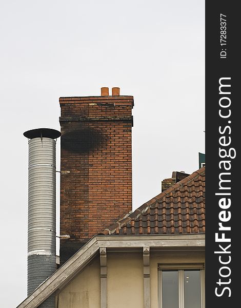 Red brick chimney and metal chimney on tiled roof