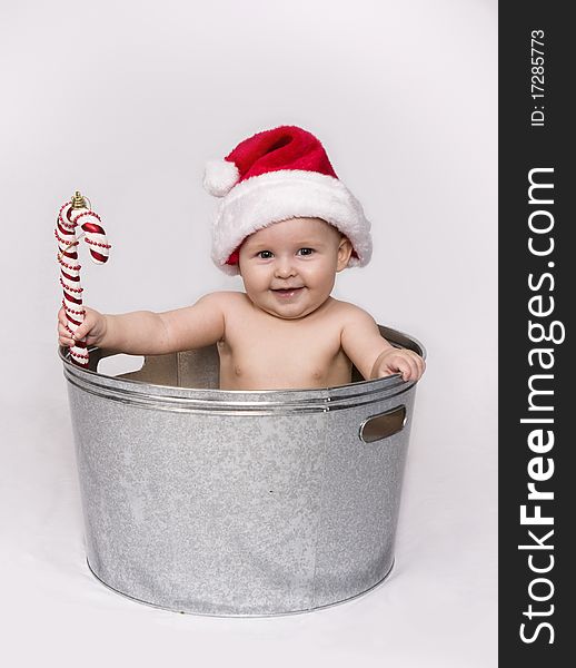 Baby holding a candy cane ornament, wearing a Santa hat, and sitting in a wash basin. Baby holding a candy cane ornament, wearing a Santa hat, and sitting in a wash basin.