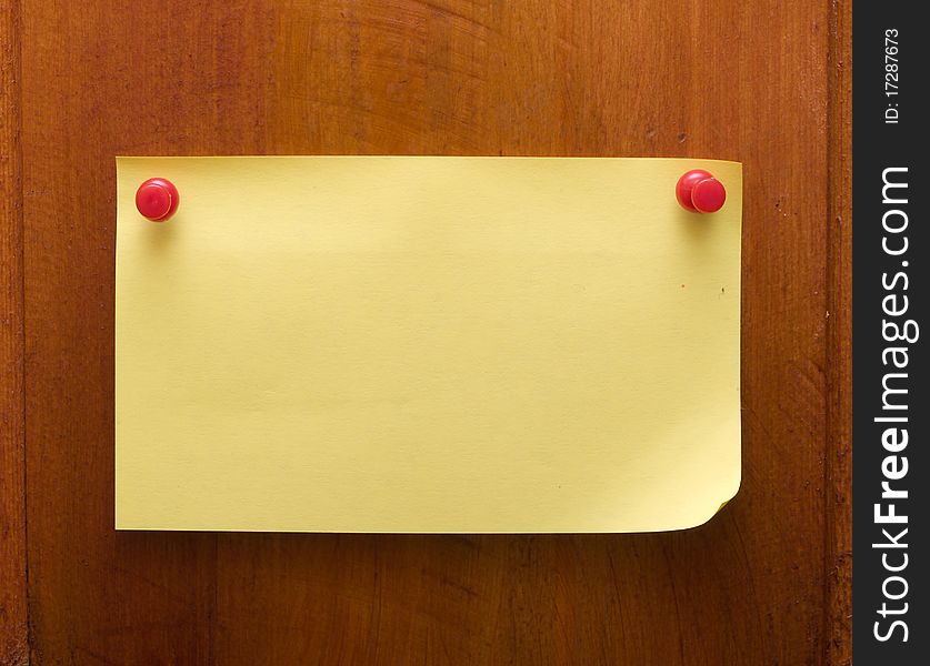 Yellow blank reminder on a wood desk with red push pin
