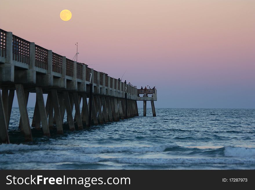 Full moon rising over the ocean and pier with colorful sky. Full moon rising over the ocean and pier with colorful sky