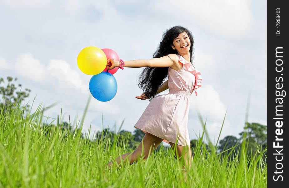 Teenage girl laughing and running holding a bunch of colorful balloons in green meadow. Teenage girl laughing and running holding a bunch of colorful balloons in green meadow