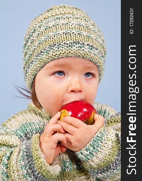 A young Boy is eating an Apple in Winter. Isolated in Studio on Blue Background.