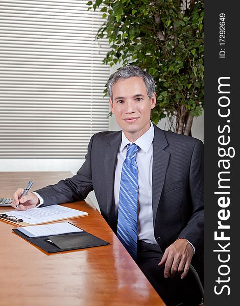 A business man in a suit takes notes while at a desk or meeting table. A business man in a suit takes notes while at a desk or meeting table