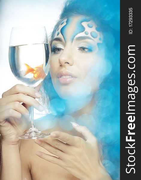 The image of a girl with makeup with a fish in a glass in her hand. The image of a girl with makeup with a fish in a glass in her hand