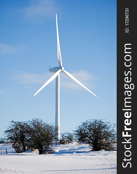 A vertical image of a snow covered field and a wind turbine