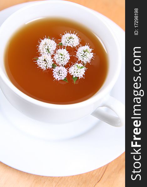 Cup of green tea with flowers of peppermint floating in it on a wooden background