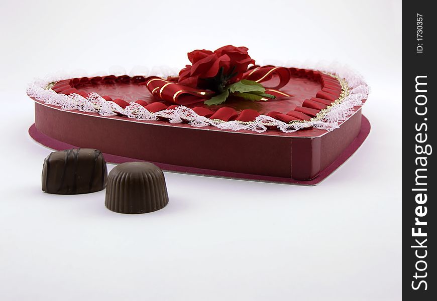 Photo of a box of valentine chocolates in a heart shape with two chocolates outside the box.